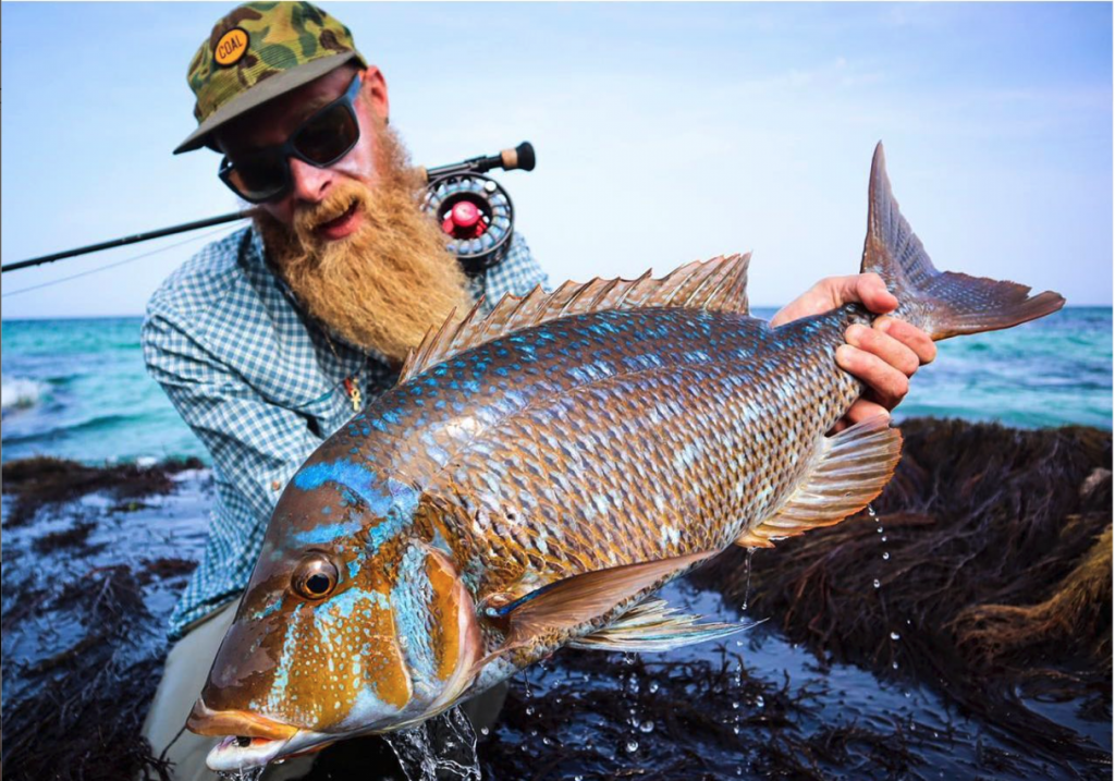 Fly Fisherman with a long red beard wearing Smith Longfin sunglasses holding a large fish balancing his fly fishing rod on his shoulders | Best fly fishing sunglasses | Jumping Rise