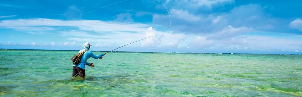 Fly fisherman wearing Maui Jim Southern Cross sunglasses and a blue shirt casting a line over a green-blue ocean on a clear sunny day.