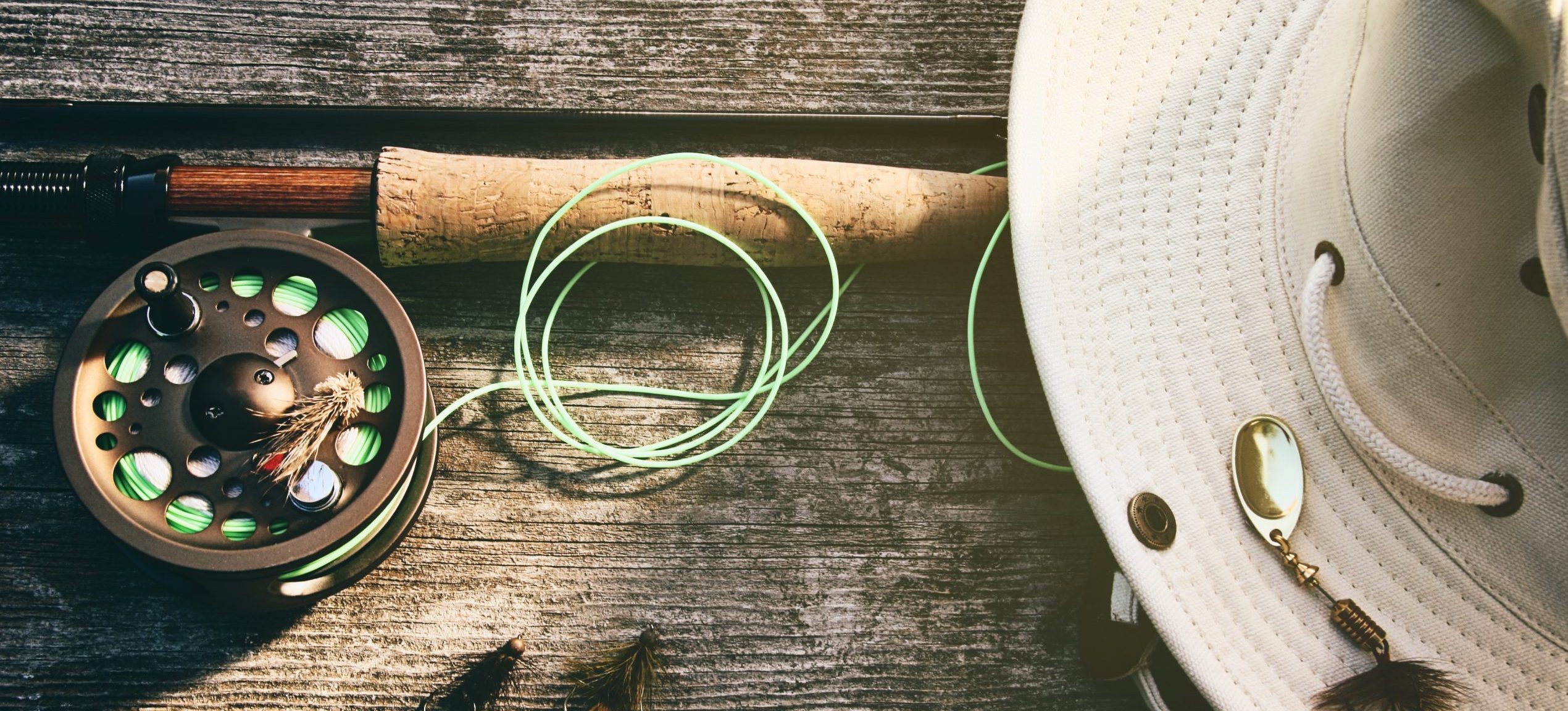 Jumping Rise: Fly fishing rod with hat on wood.